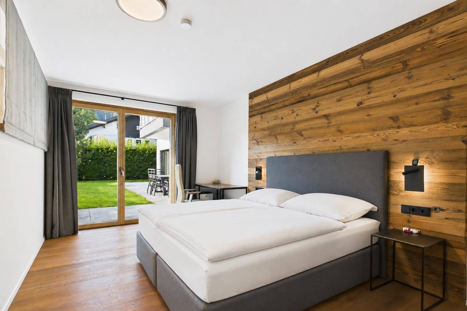 Helles Schlafzimmer mit Holzwand, Doppelbett und direktem Zugang zu einer Terrasse oder Garten.
