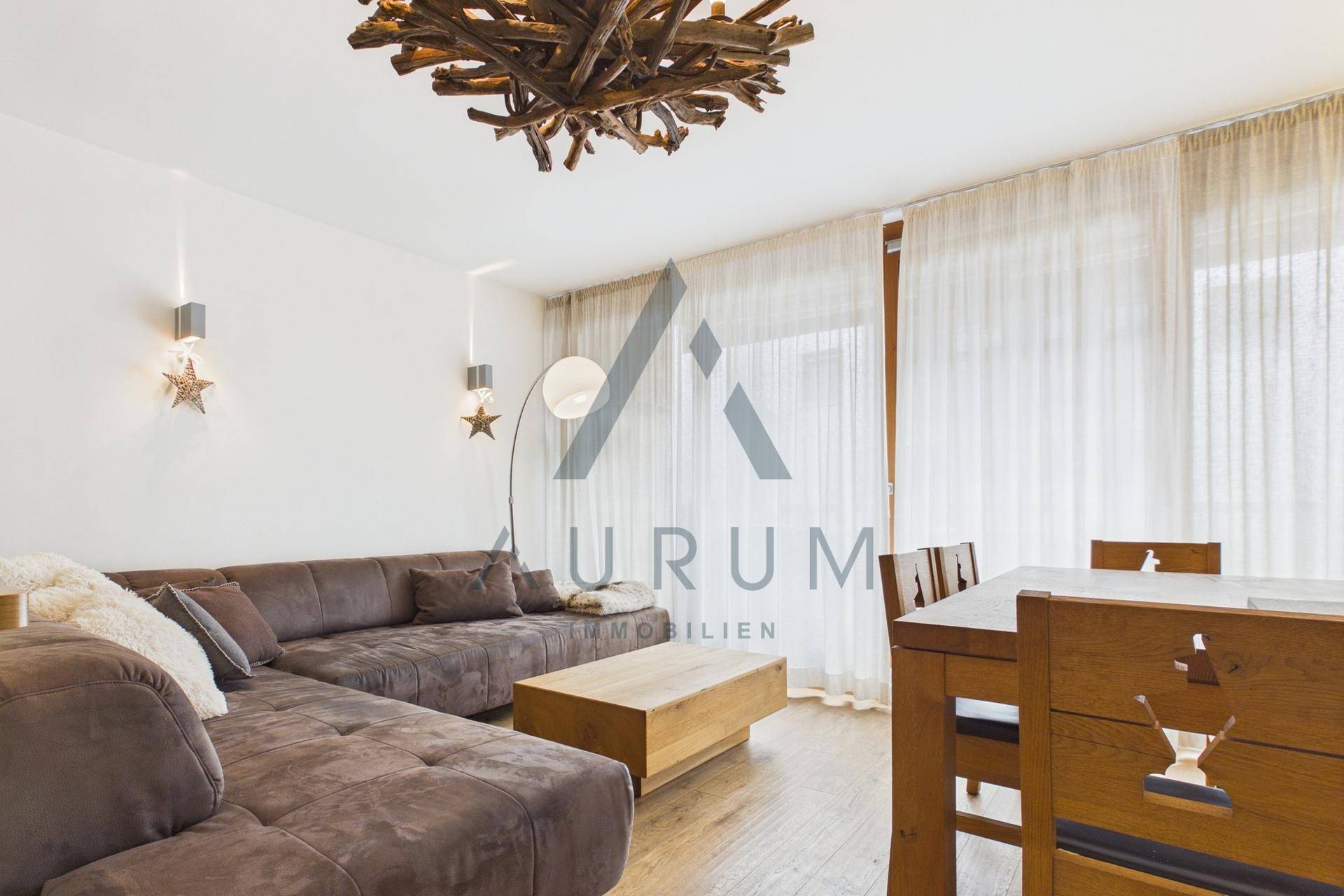 Gemütlicher Wohnbereich mit großem Ecksofa, Holztisch und hellen Vorhängen.