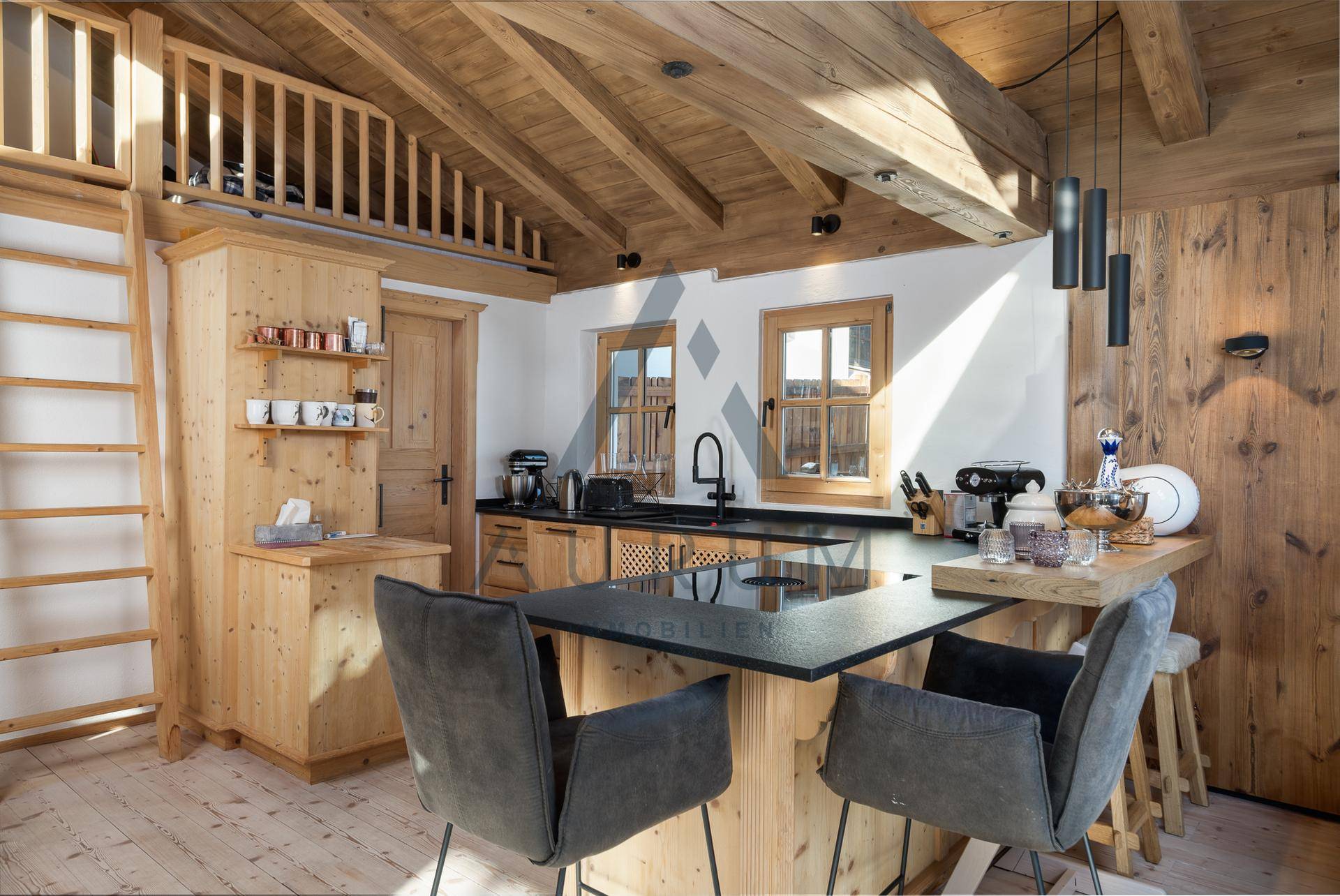Rustikale Holzküche mit moderner Ausstattung, Kücheninsel und Dachschrägen, die zum Loftbereich führen.