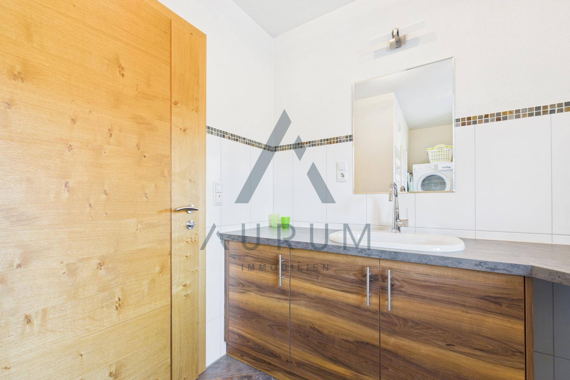 Badezimmer mit Waschbecken, Holzschrank und Spiegel, daneben eine Holztür.