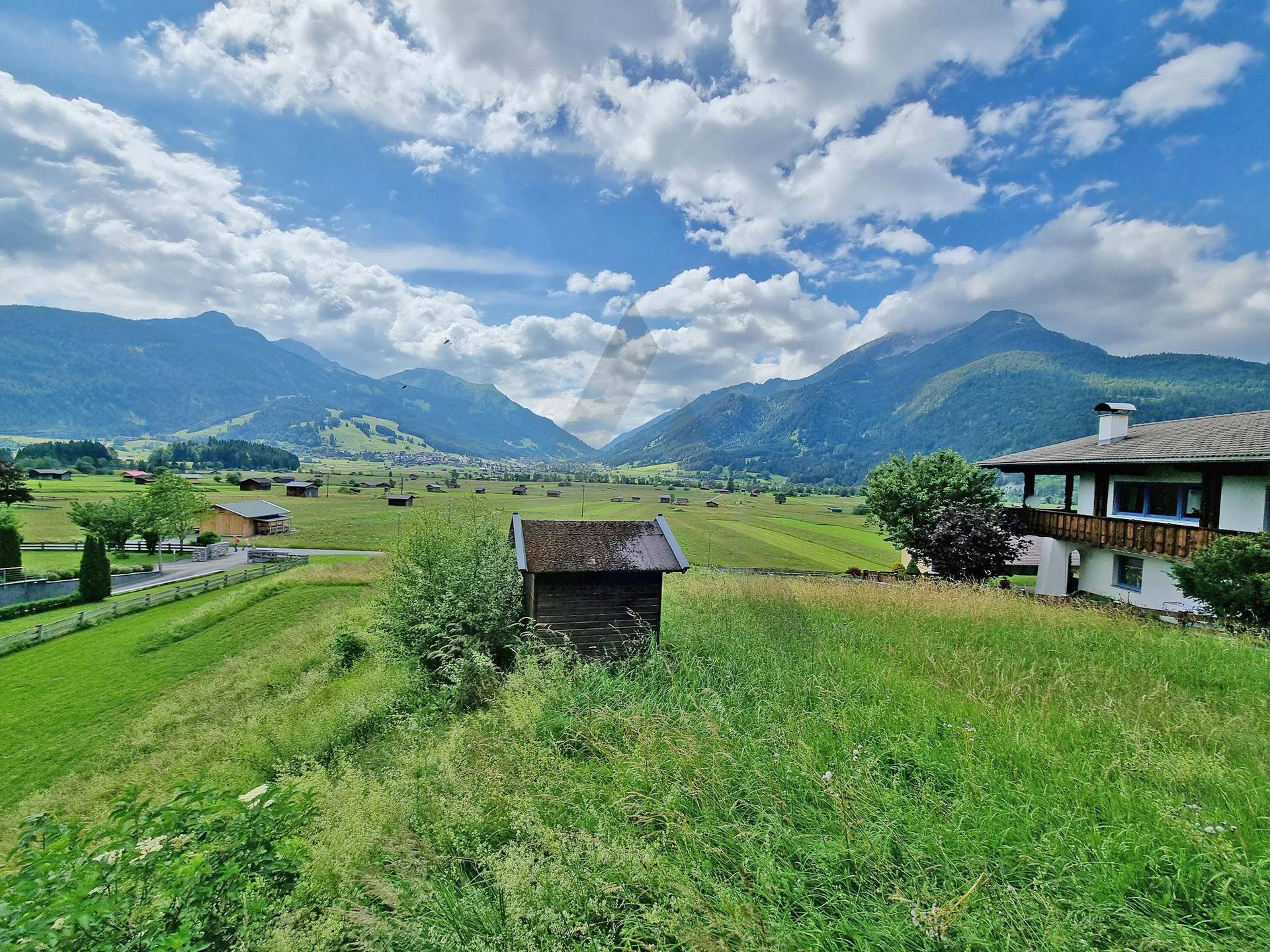 Idyllischer Ausblick auf die Alpenlandschaft mit einem kleinen Holzschuppen und einem traditionellen Haus.