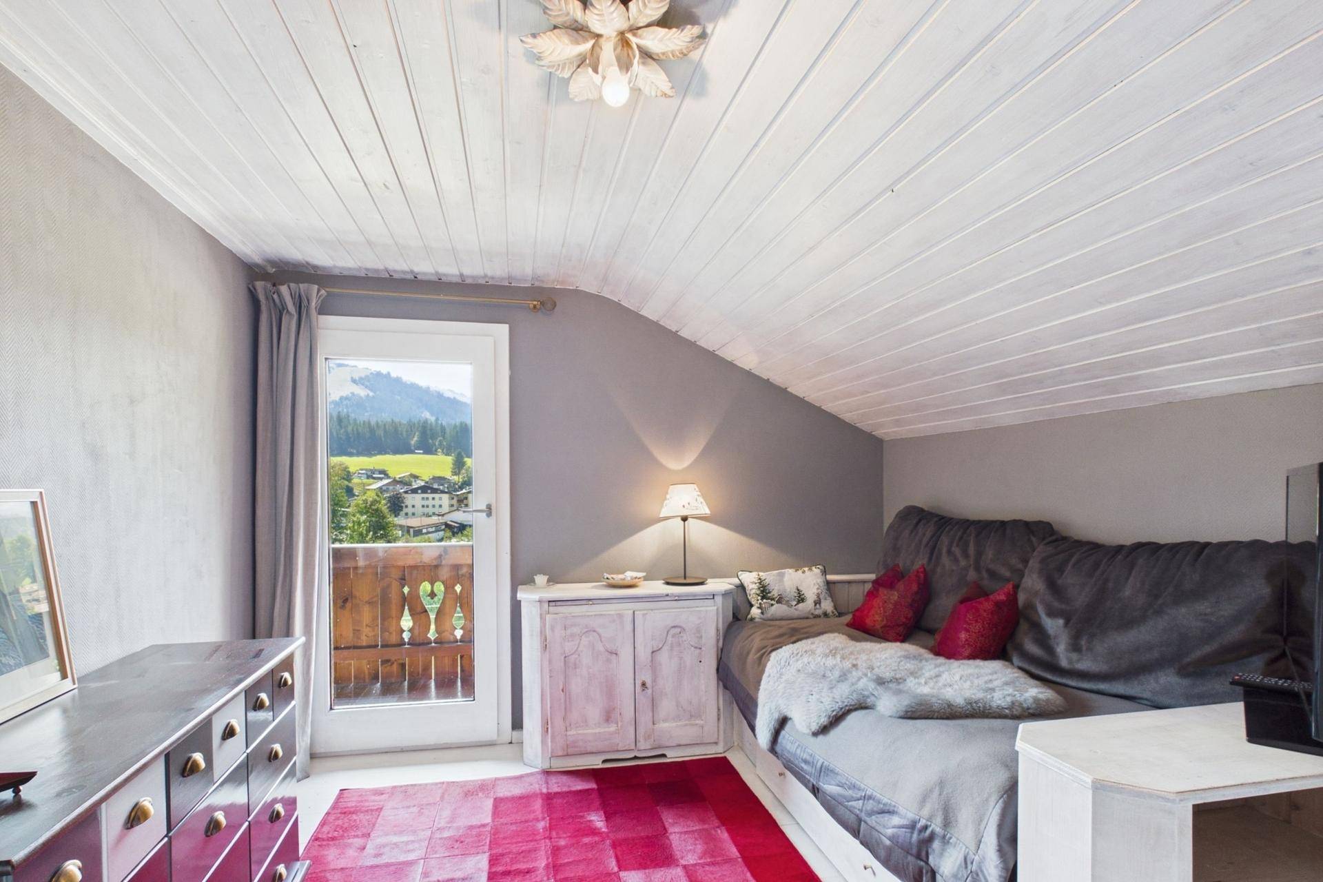 Gemütliches Schlafzimmer im Dachgeschoss mit Tagesbett, Holzdecke und Balkonzugang mit Bergblick.