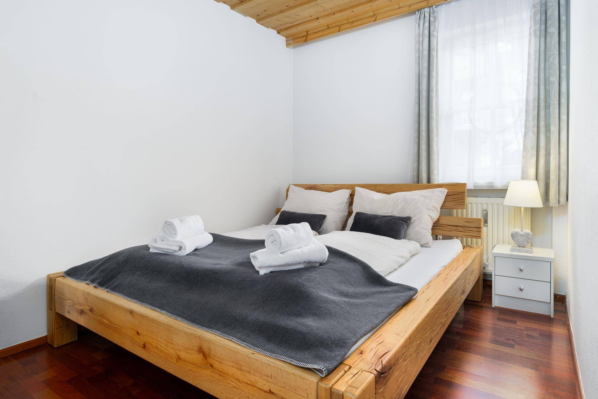Schlafzimmer mit rustikalem Holzbett, Holzbalkendecke und Fenster für natürliches Licht.