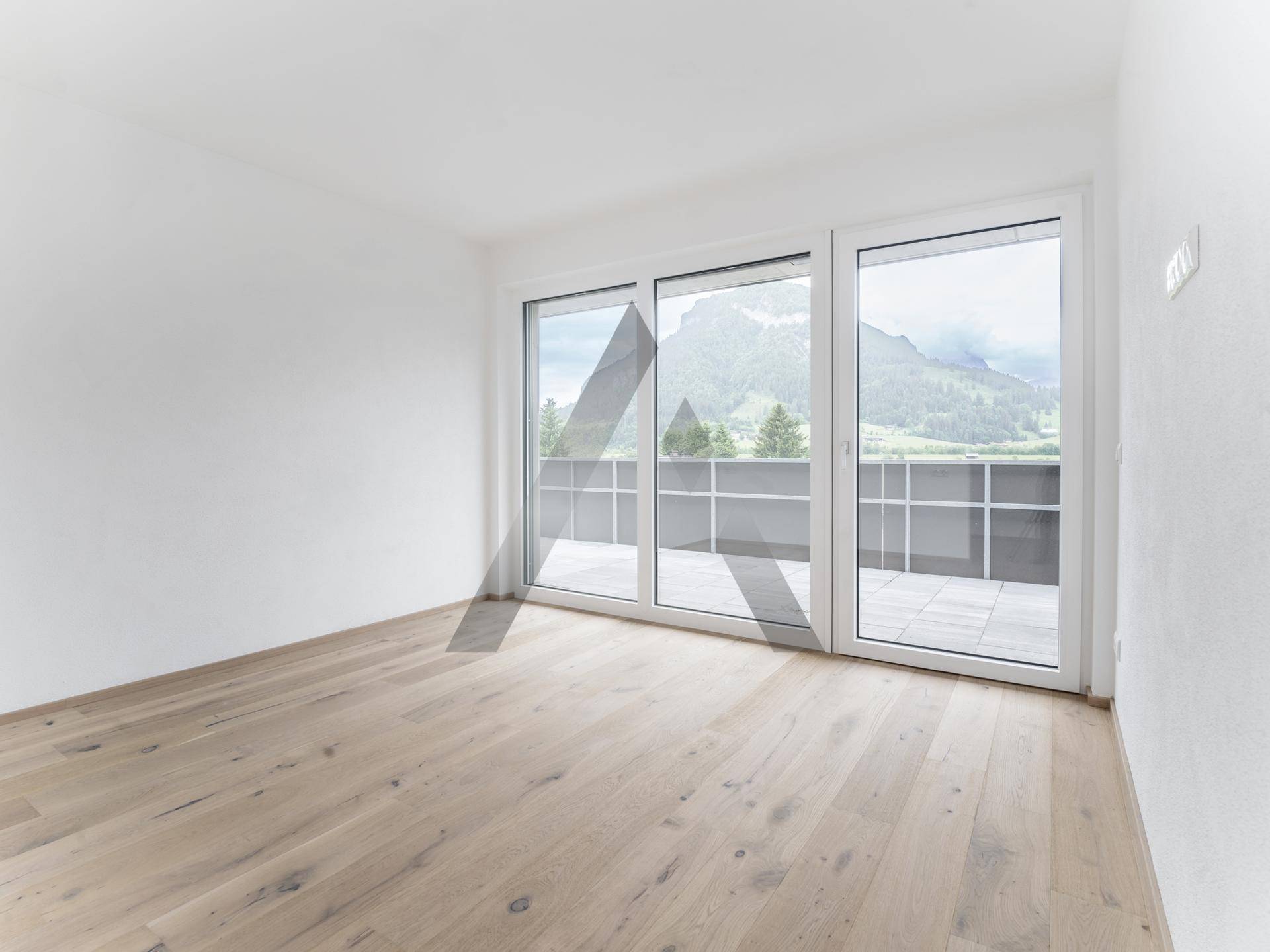 Helles Schlafzimmer mit Holzboden und großen Fenstern, die einen weiten Blick auf die Berge ermöglichen.