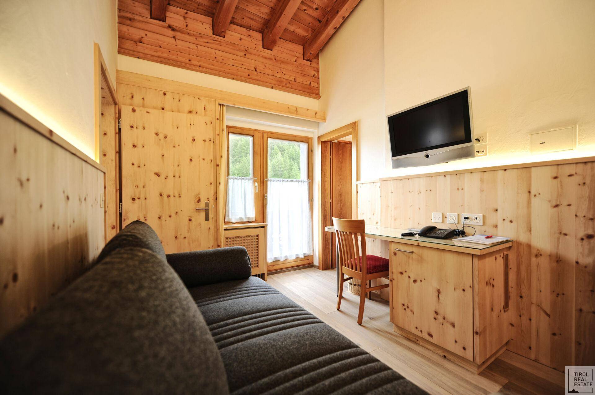 Schlafzimmer mit Holzwänden, einem Schreibtischbereich und einem Sofa, ideal für Arbeit und Entspannung.