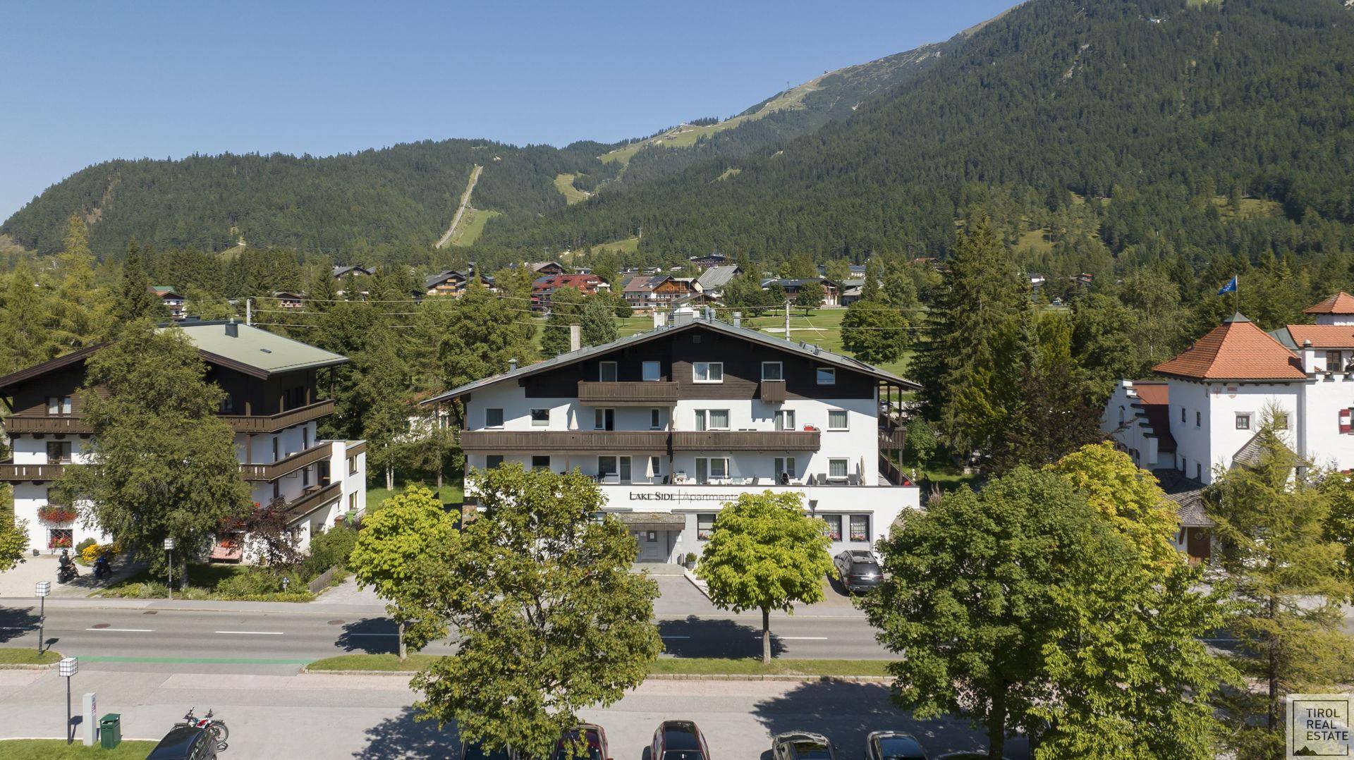 Ansicht des Gebäudes mit umliegender Natur, Bäumen und Bergen im Hintergrund.