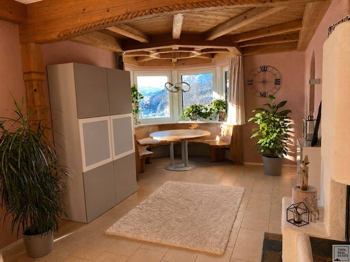 Gemütlicher Essbereich mit rustikaler Holzeckbank, rundem Tisch und Blick auf die grüne Landschaft durch das Fenster.
