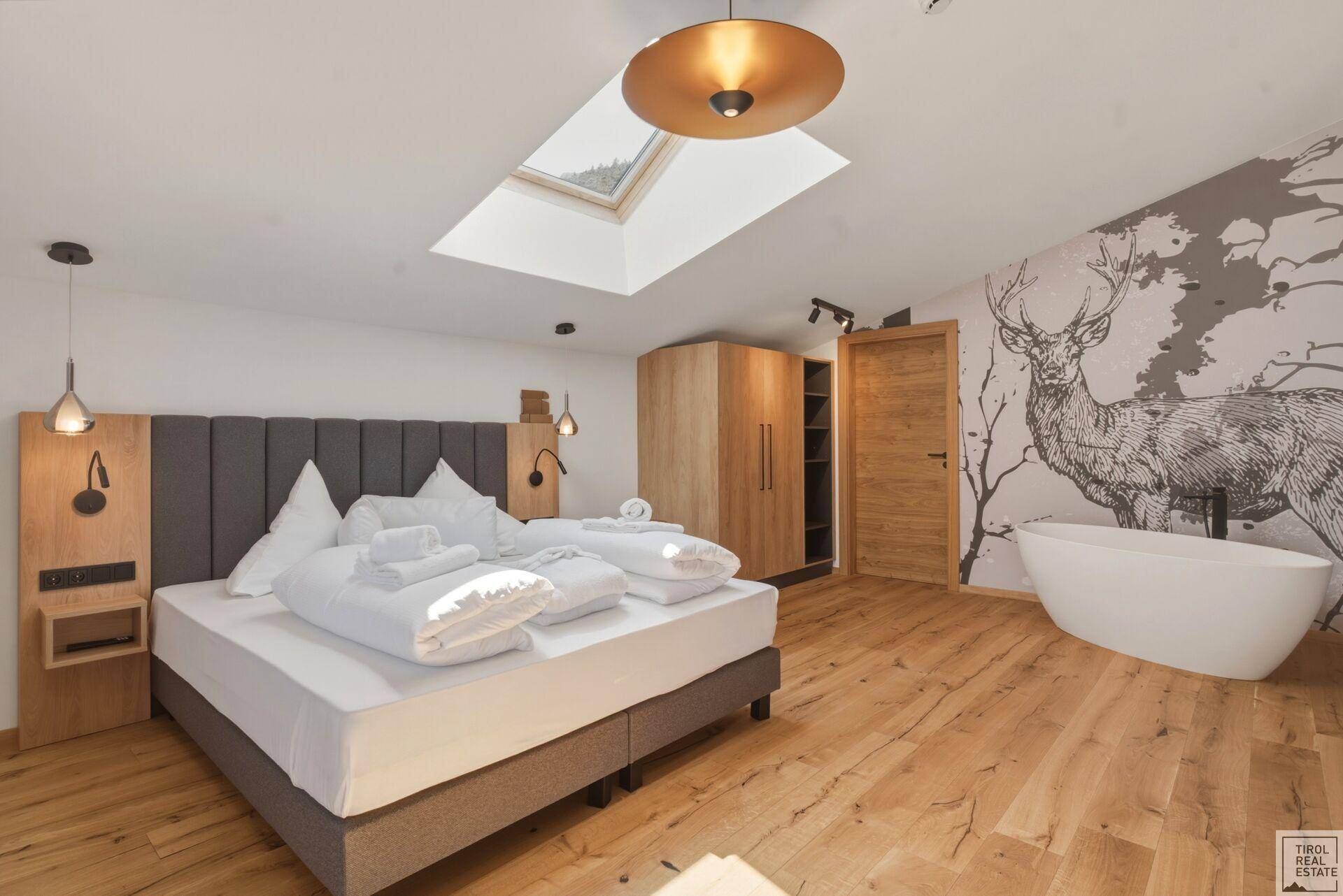 Modernes Schlafzimmer mit Holzboden, freistehender Badewanne und Hirschmotiv an der Wand.