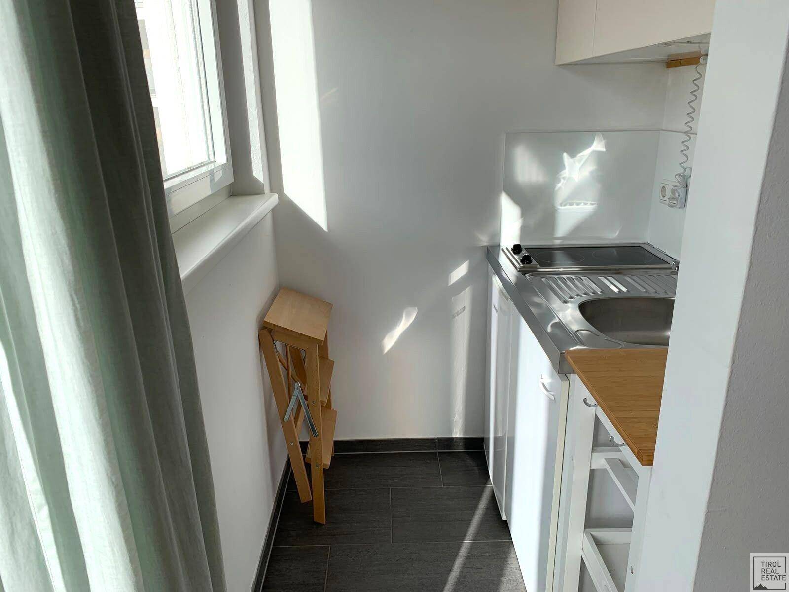 Kompakte Küchenzeile mit Spüle, Kochfeld und Fenster, ideal für kleine Wohnungen.