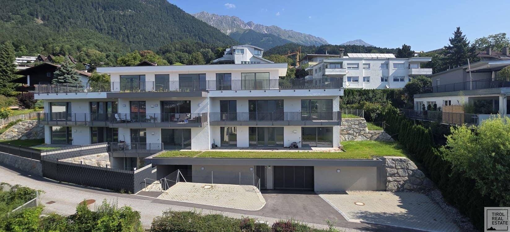 Modernes Mehrfamilienhaus mit Flachdach und großen Fensterfronten in alpiner Umgebung mit Bergblick.