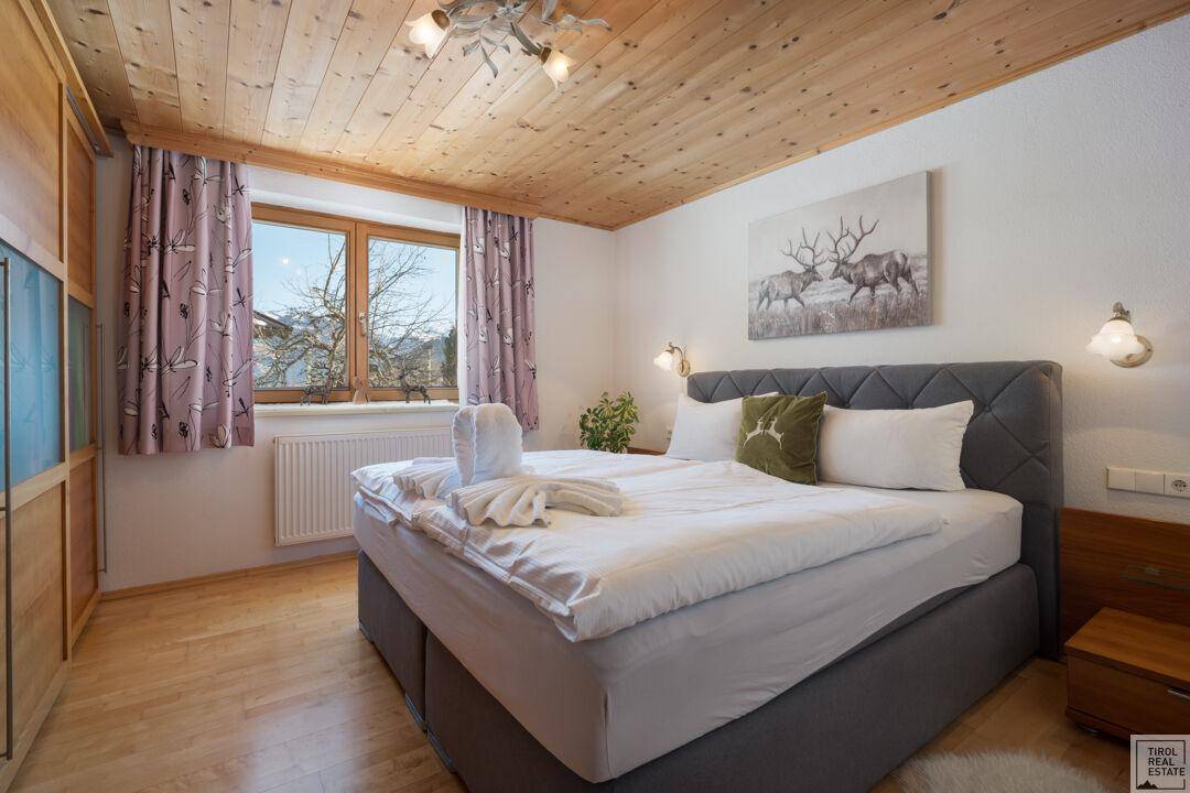 Gemütliches Schlafzimmer mit Holzbalkendecke, Parkettboden und Bergblick durch das Fenster.