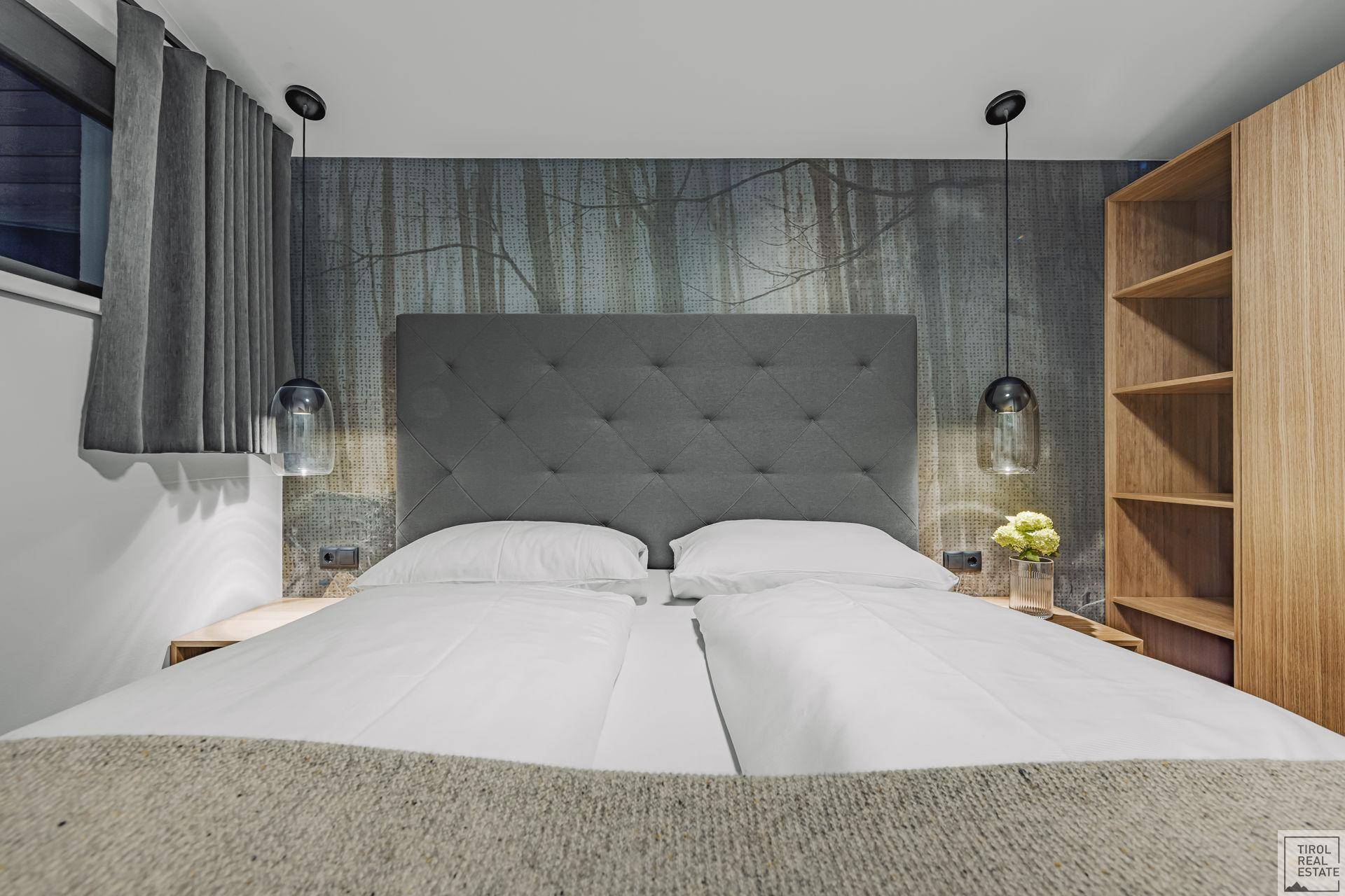 Gemütliches Schlafzimmer mit großem Bett, Holzelementen und einer stilvollen Wandtapete mit Waldmotiv.