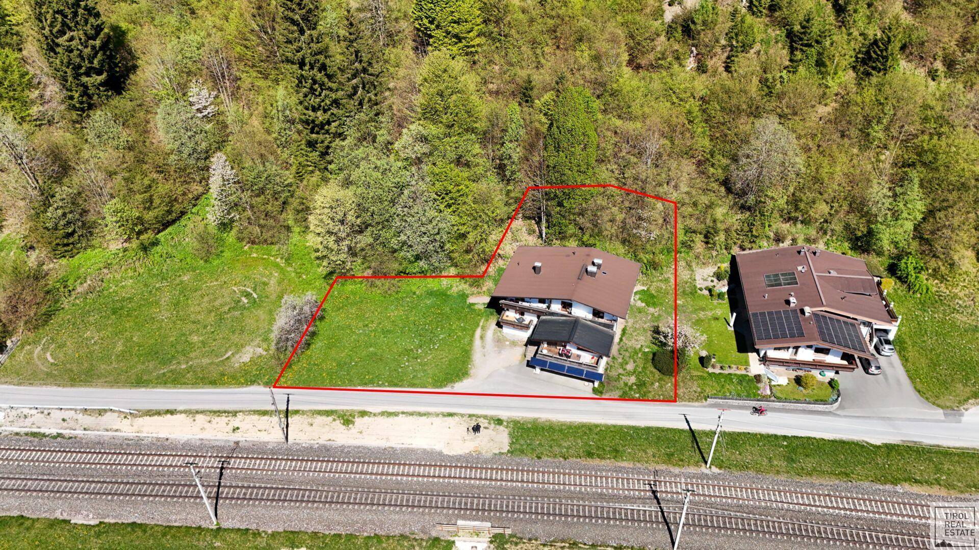 Luftaufnahme des Grundstücks mit Wohnhaus, umgeben von Wald und einer Bahnlinie in den Bergen.
