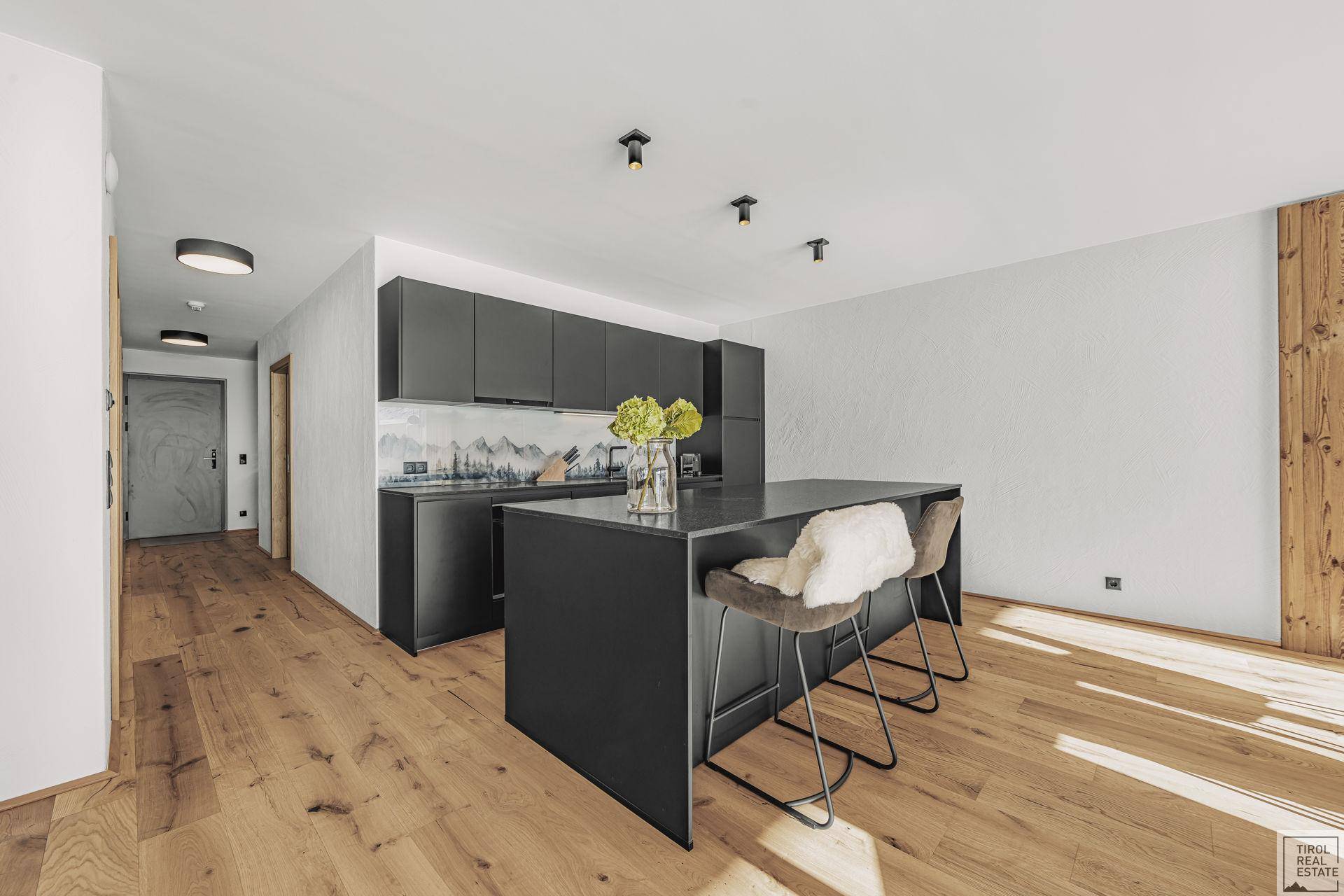 Moderne schwarze Küche mit Kochinsel, Holzboden und Zugang zum Flur.