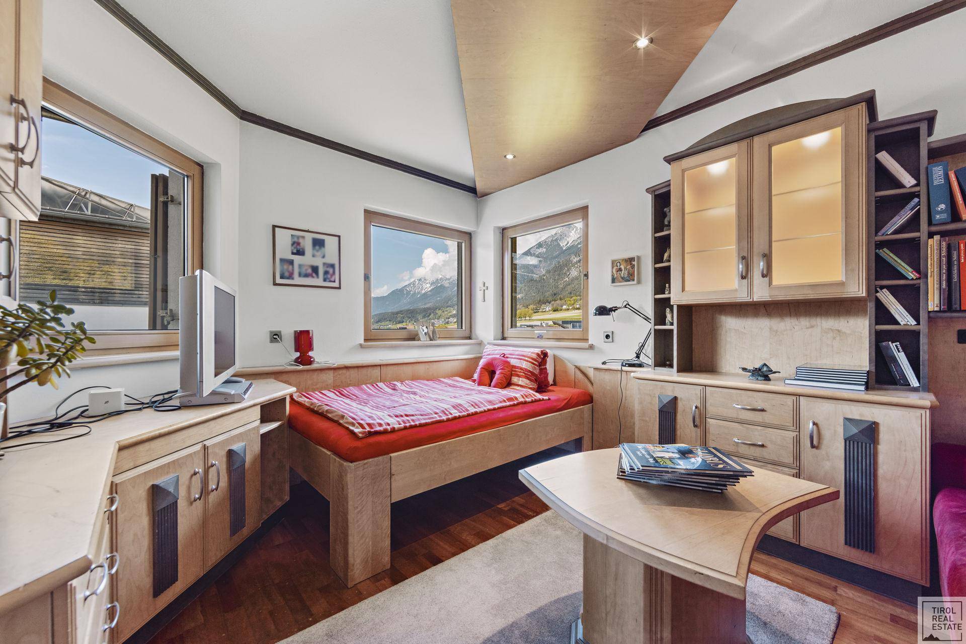 Gemütliches Schlafzimmer mit Einzelbett, Schreibtisch und Einbaumöbeln aus Holz mit Bergblick.
