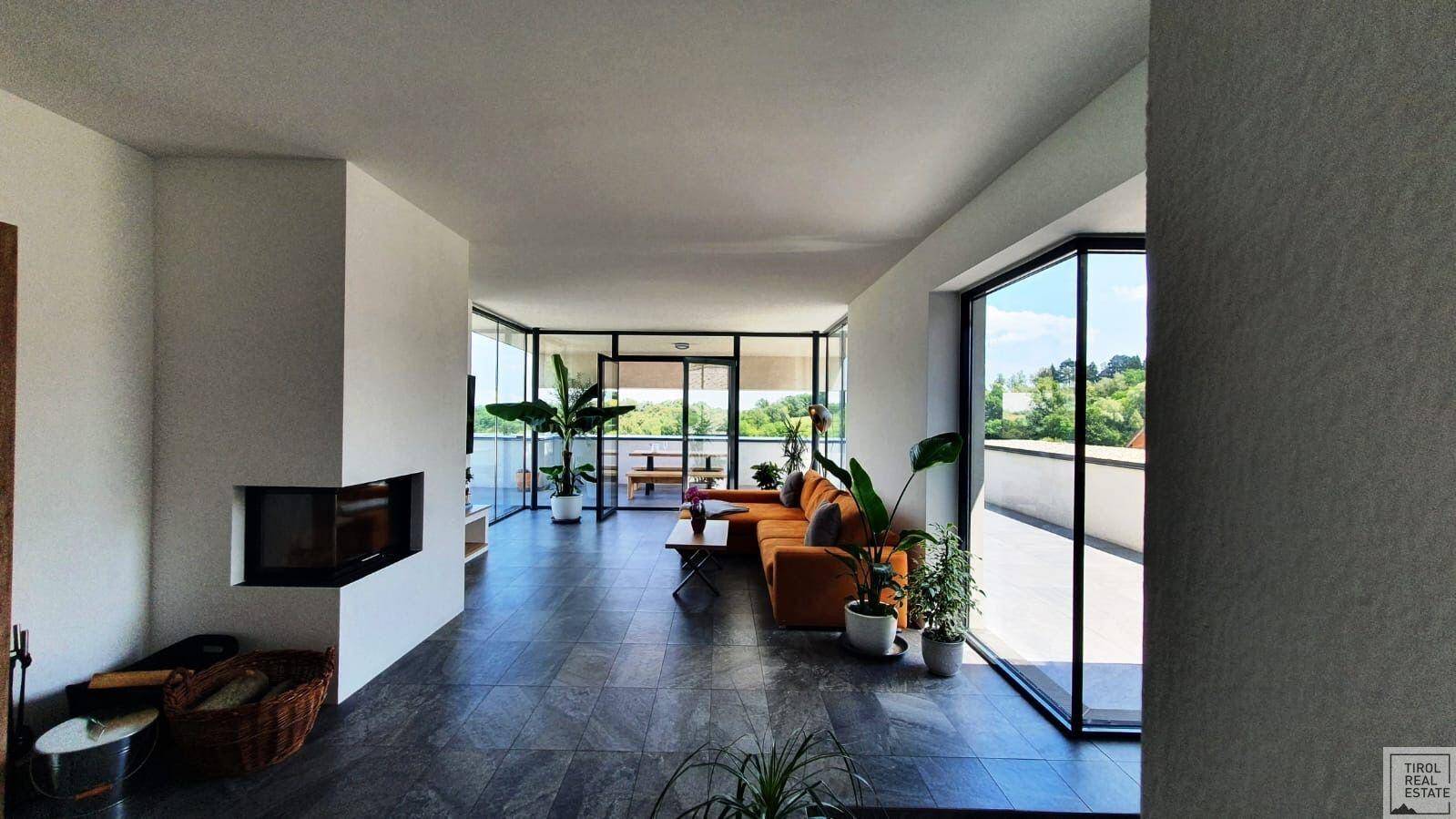 Geräumiges Wohnzimmer mit großen Fenstern, Kamin und Blick auf die grüne Umgebung, ausgestattet mit modernen Fliesen.