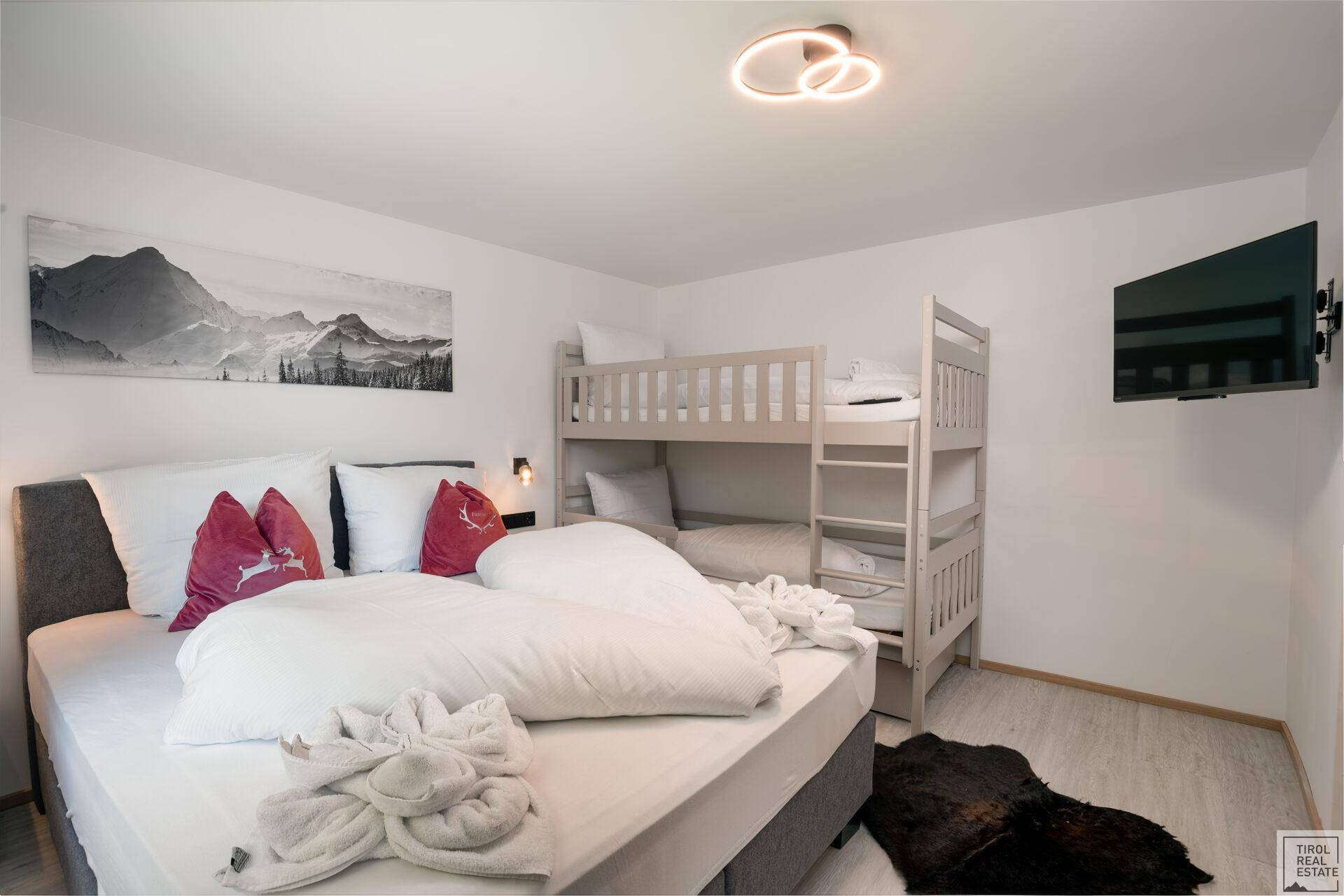 Helles Schlafzimmer mit Doppelbett, Etagenbett und moderner Wanddekoration für Gäste.