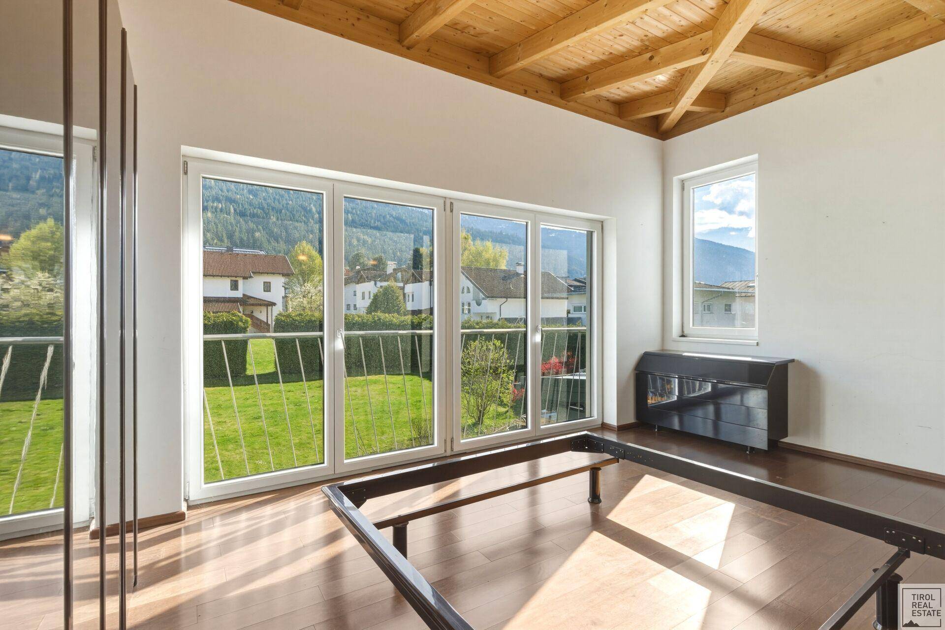 Schlafzimmer mit Holzboden, großen Fenstern und Blick auf den Garten und die umliegende Landschaft.