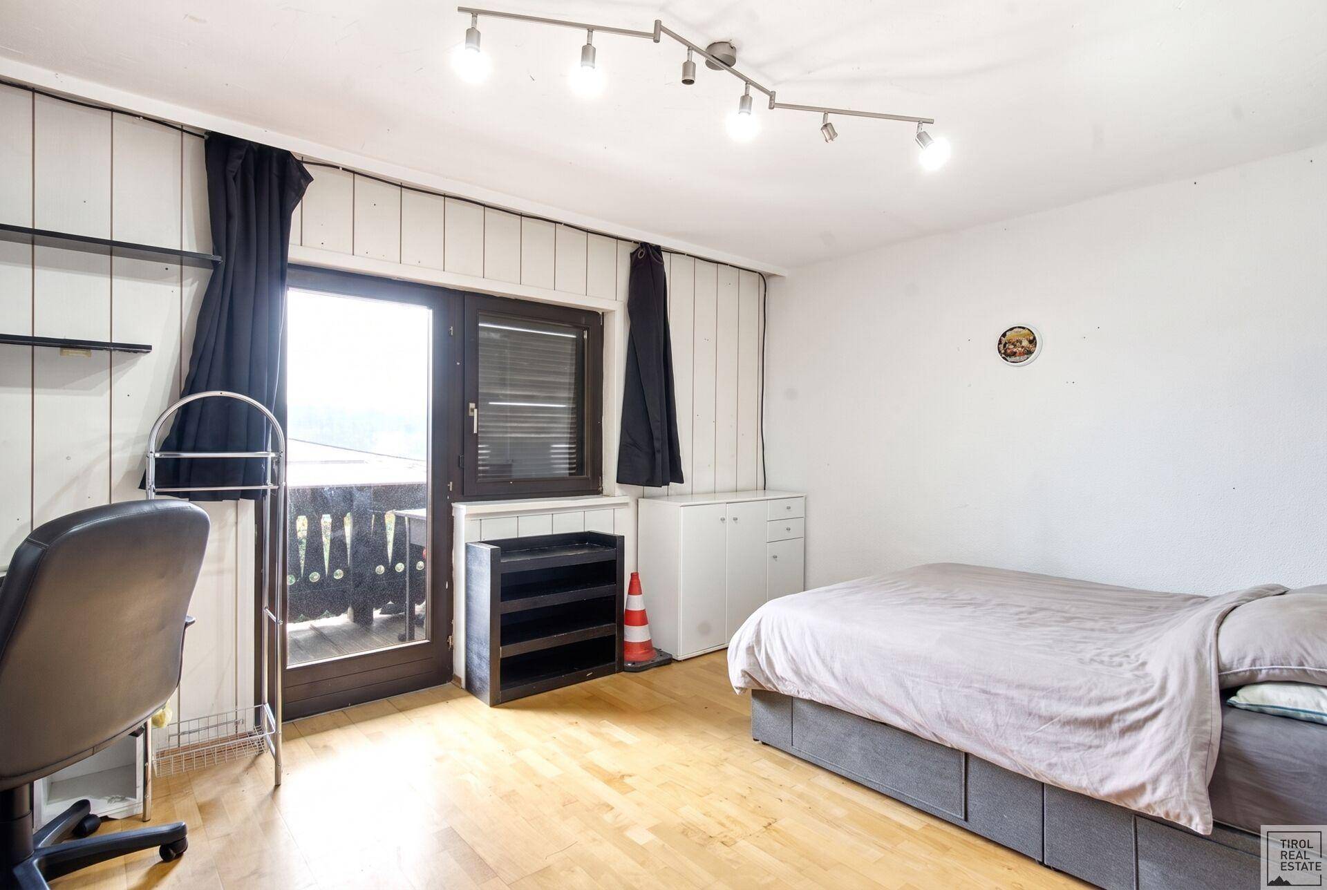 Schlafzimmer mit hellem Holzboden, weiß gestrichenen Wänden und Balkonzugang.
