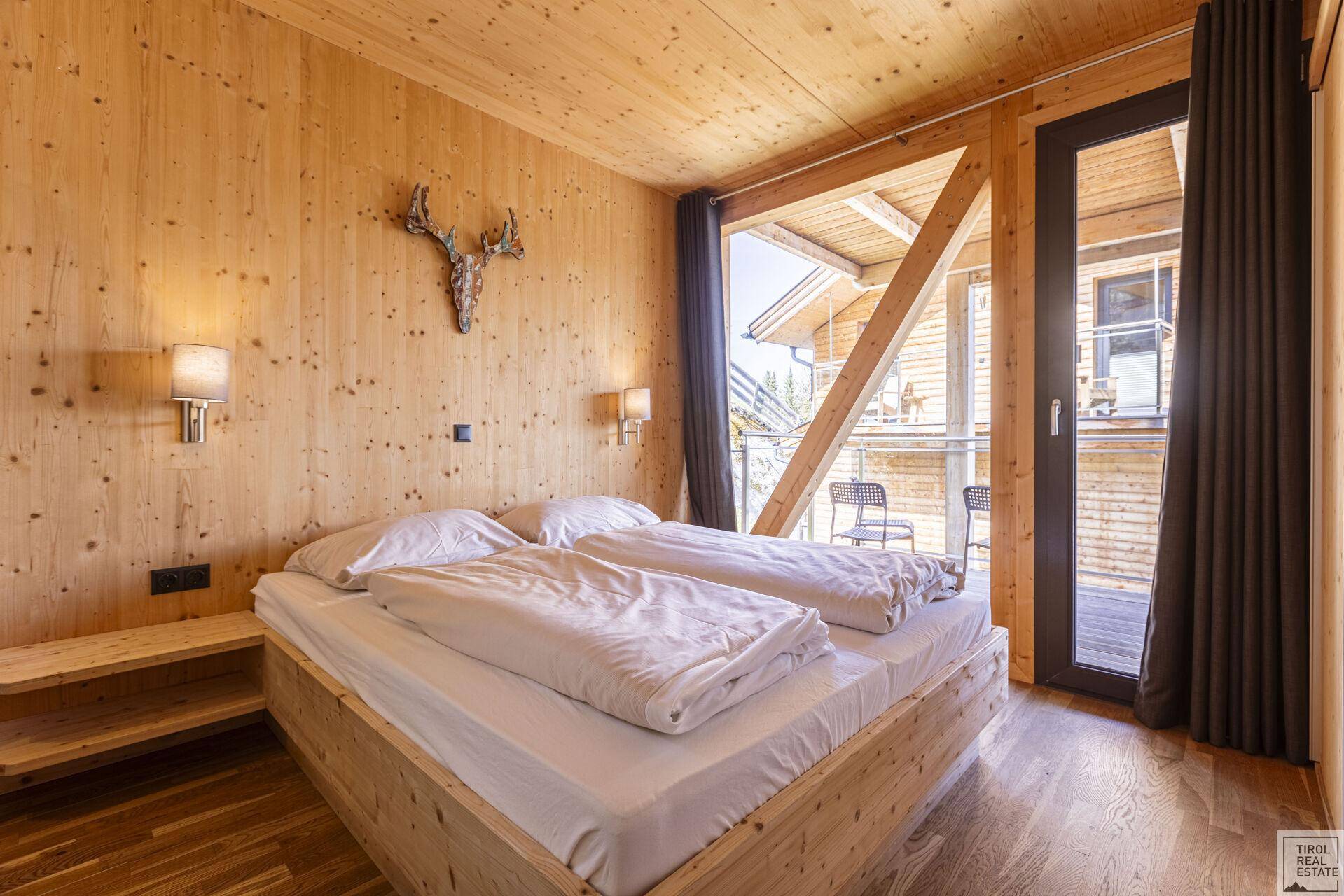 Gemütliches Schlafzimmer mit Holzeinrichtung, Doppelbett und Balkonzugang mit Bergblick.