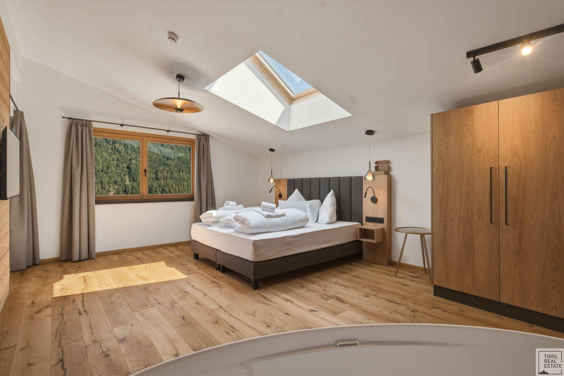 Helles Schlafzimmer mit Holzboden, Dachfenster und Blick auf die umliegende Berglandschaft.