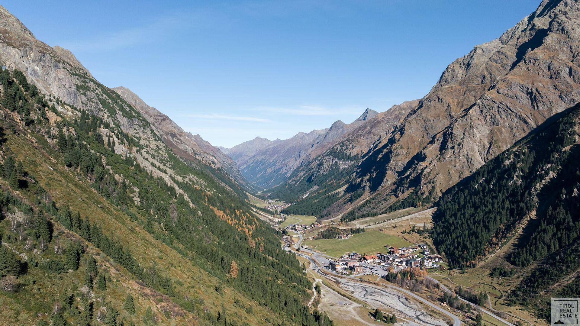 Weites Tal in den Alpen mit einem kleinen Dorf und majestätischen Bergen.