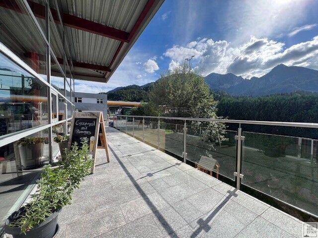 Außenterrasse mit modernem Glasgeländer und weitem Blick auf die Berge und die grüne Umgebung.