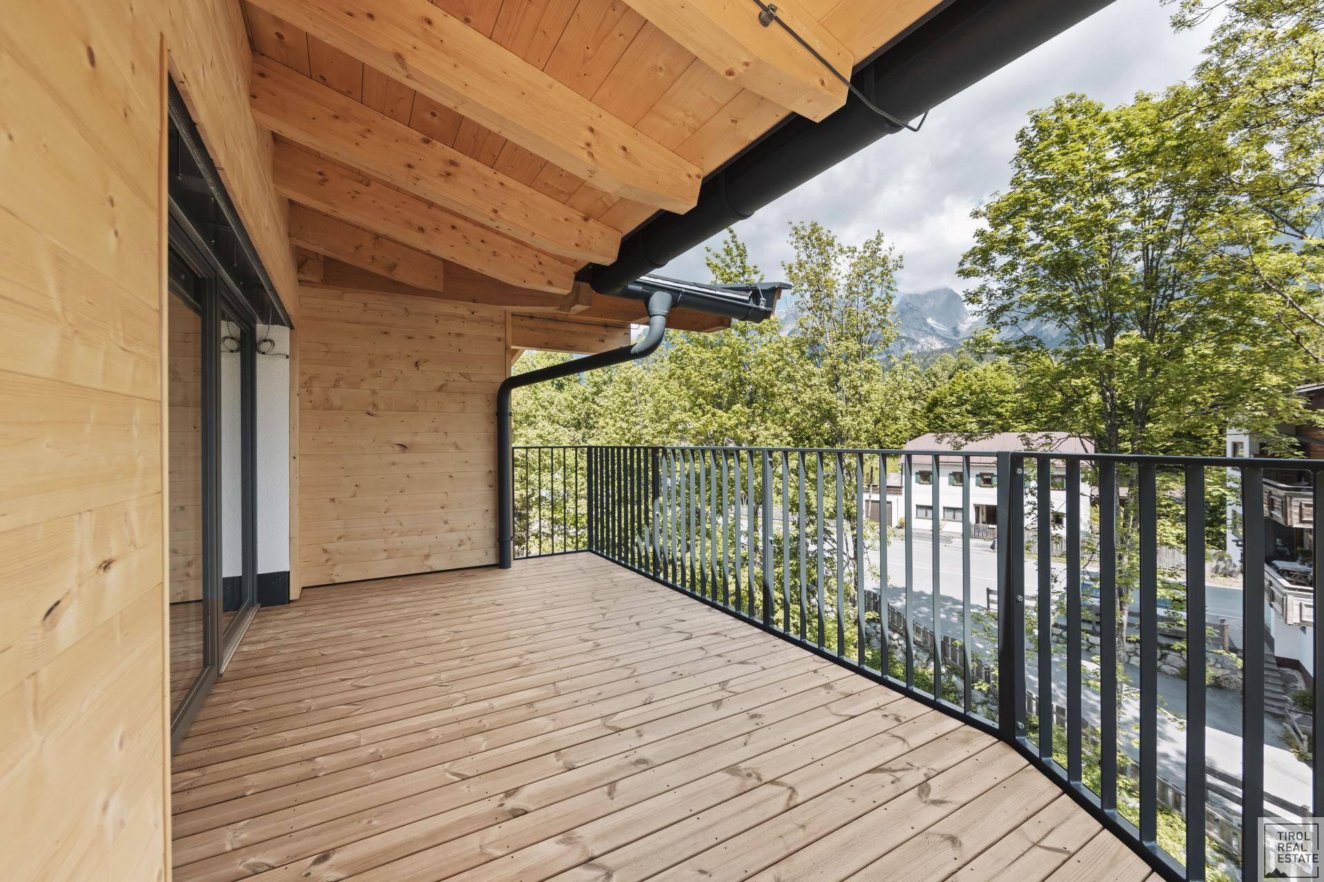 Geräumiger Holzbalkon mit schwarzem Geländer und beeindruckendem Blick auf die Berge.