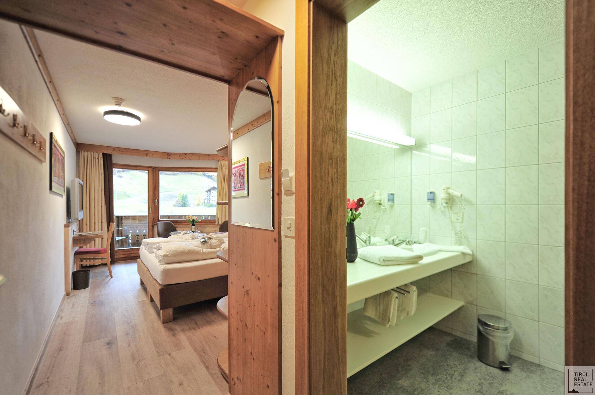 Badezimmer mit Waschtisch und Blick in ein gemütliches Schlafzimmer mit Doppelbett.