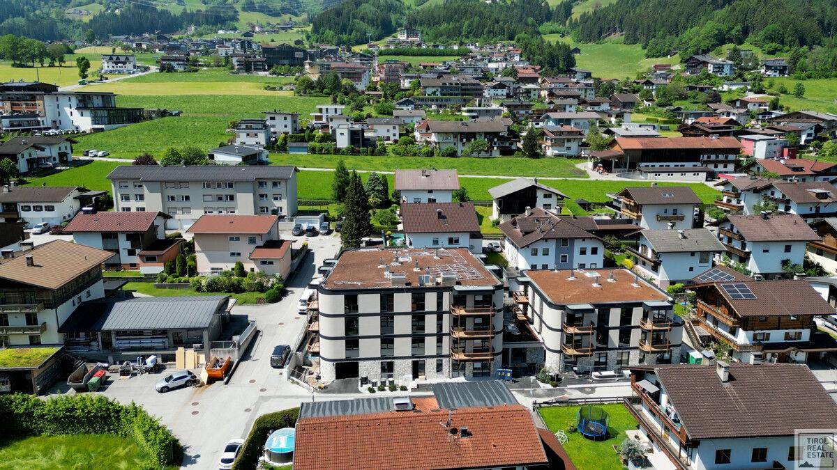 Weitläufige Luftaufnahme einer Wohnanlage eingebettet in eine grüne Landschaft mit umliegenden Bergen.