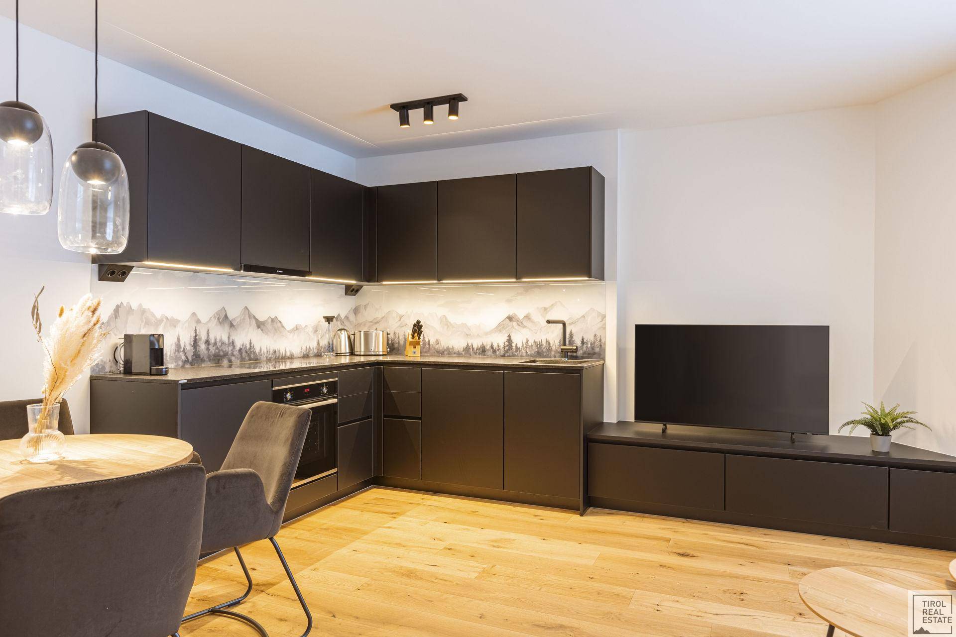 Moderne schwarze Einbauküche mit integrierten Geräten und einem Esstisch in einem offenen Wohnbereich.