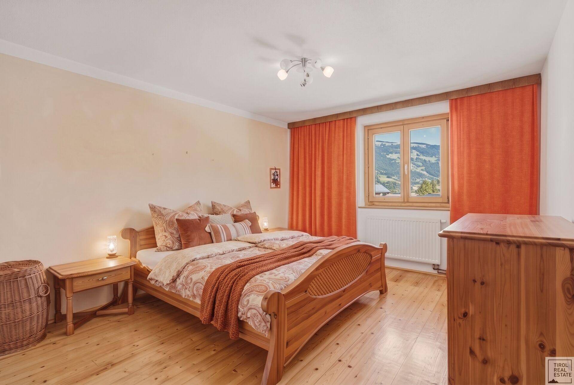 Schlafzimmer mit Holzbett, Holzkommode und Blick auf die umliegende Berglandschaft.