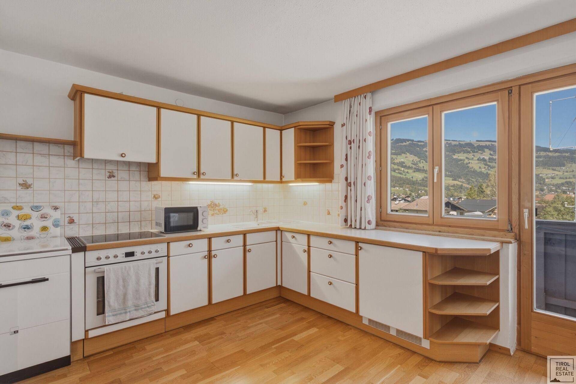 Funktionale Küche mit Holzboden, weißen Schränken und Bergblick durch das Fenster.