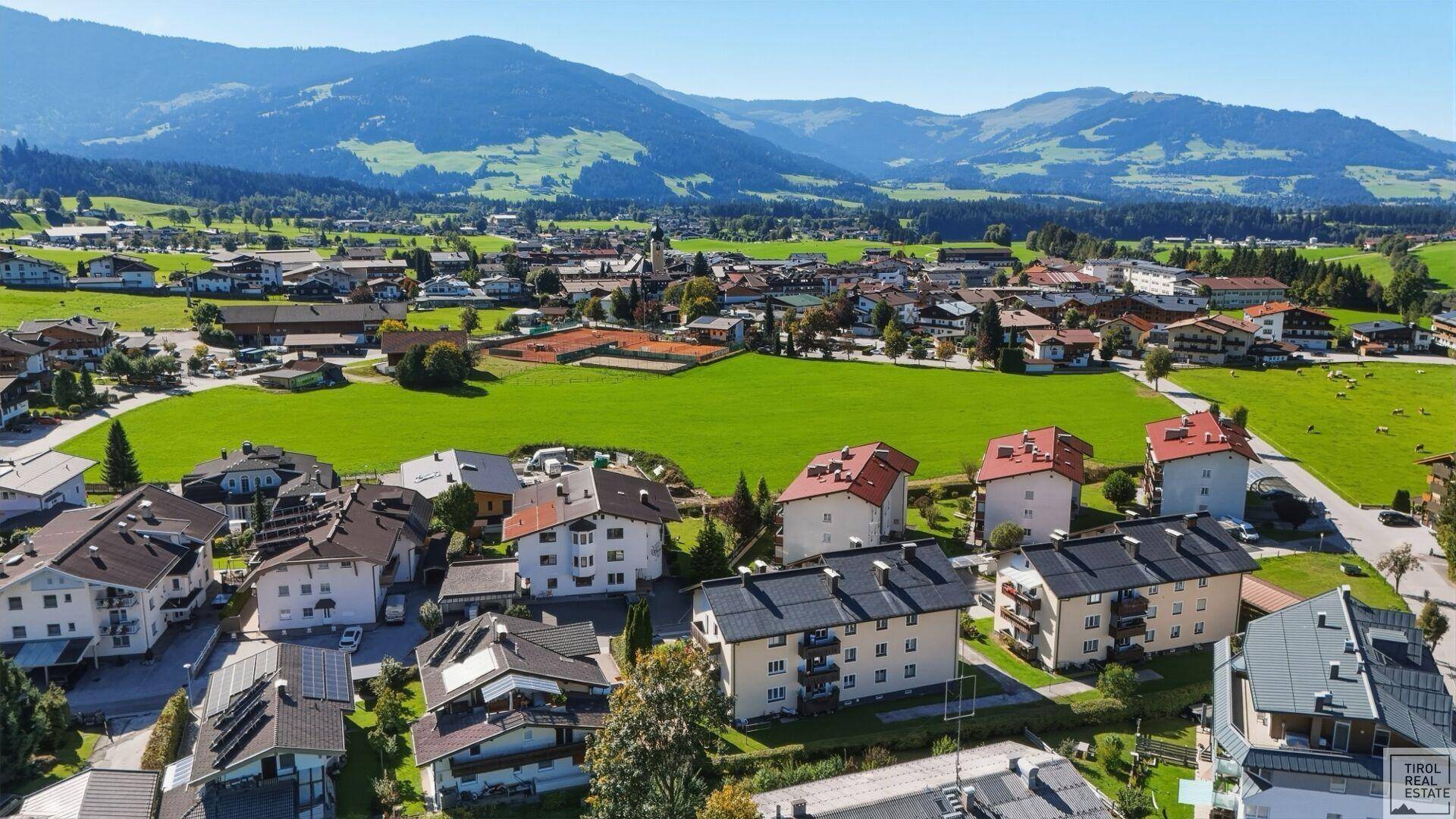 Panoramablick auf die Wohngegend mit grünen Feldern und majestätischen Bergen im Hintergrund.