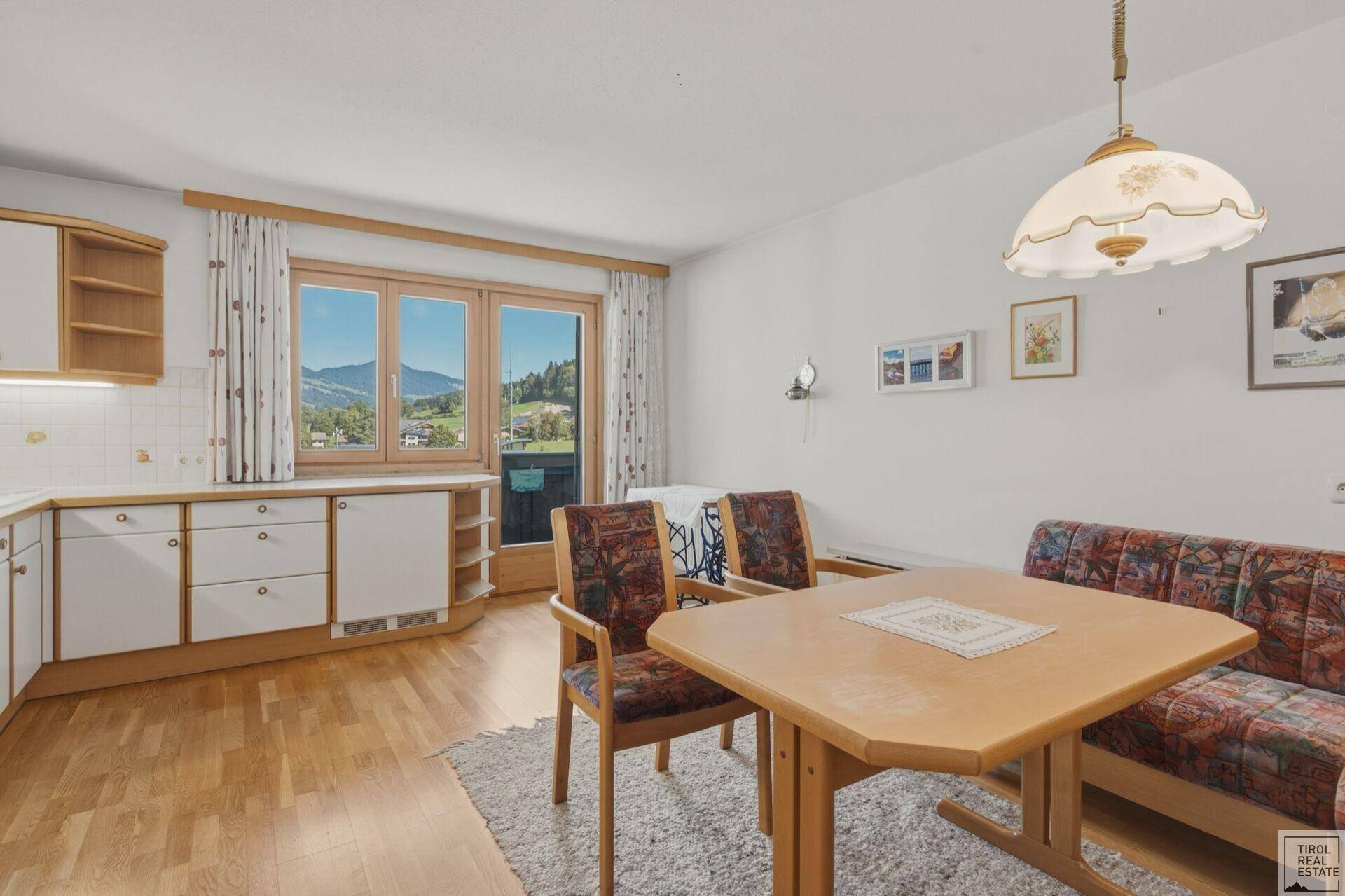 Kombinierter Wohn- und Essbereich mit Holzboden und Zugang zum Balkon mit Bergblick.
