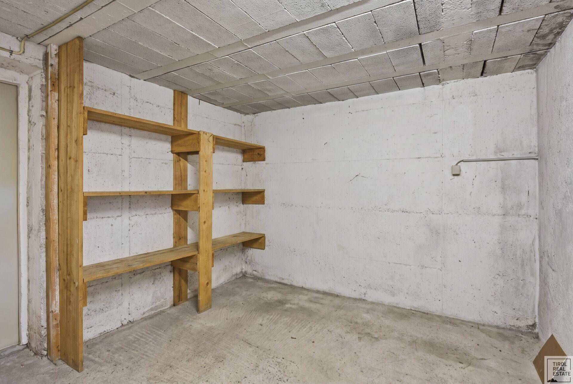 Einfacher Abstellraum im Keller mit Holzregalen und Betonwänden.