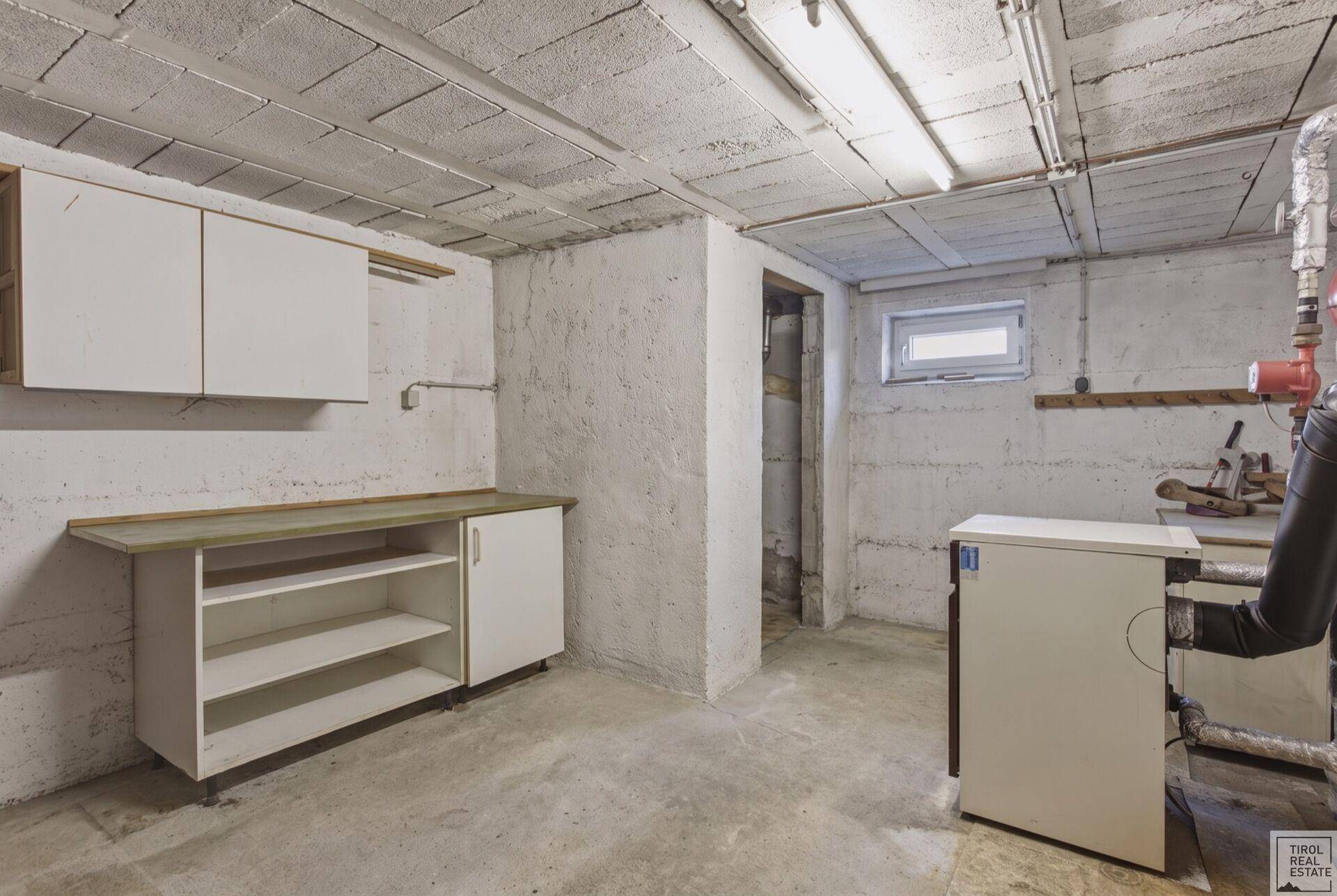 Kellerraum mit Betonboden, einfachen Schränken und einem kleinen Fenster.