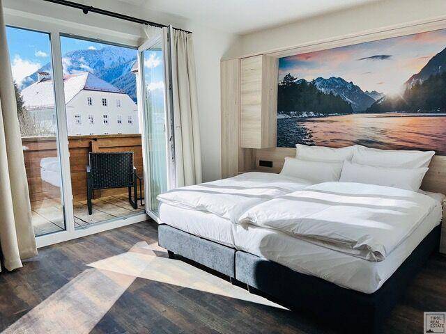 Gemütliches Schlafzimmer mit Doppelbett, Holzboden und Zugang zu einem Balkon mit Bergblick.