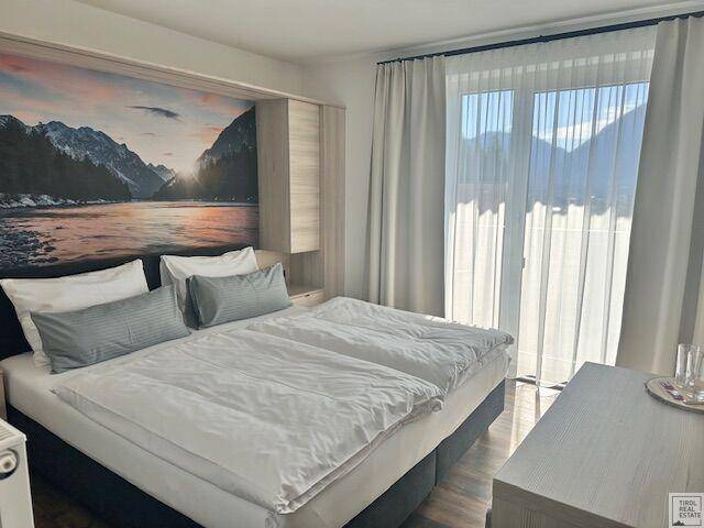 Komfortables Schlafzimmer mit Doppelbett, Vorhängen und großem Fenster mit Blick auf die Berge.