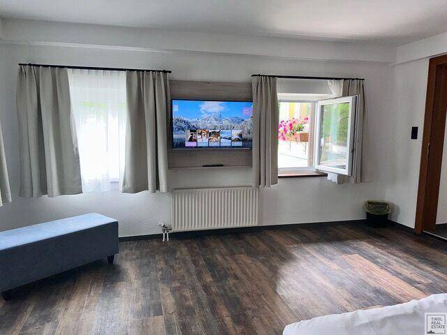 Helles Schlafzimmer mit Holzboden, Fernseher und Fenster mit Blick auf Blumenkästen.