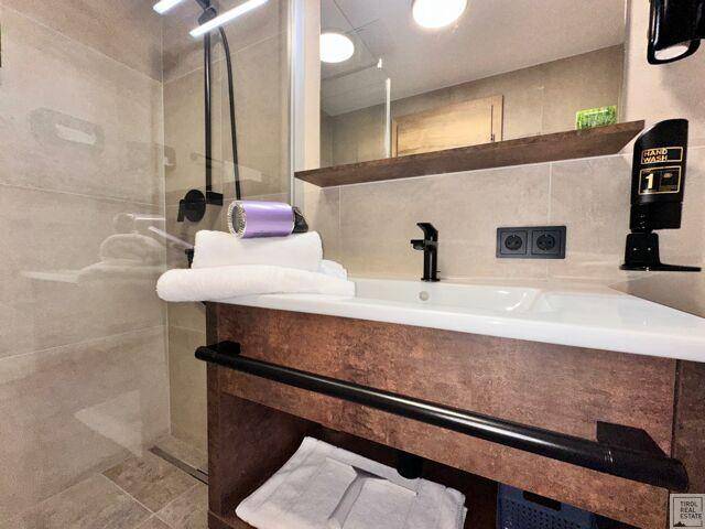 Modernes Badezimmer mit Waschtisch, Spiegel und Duschkabine mit schwarzen Armaturen.