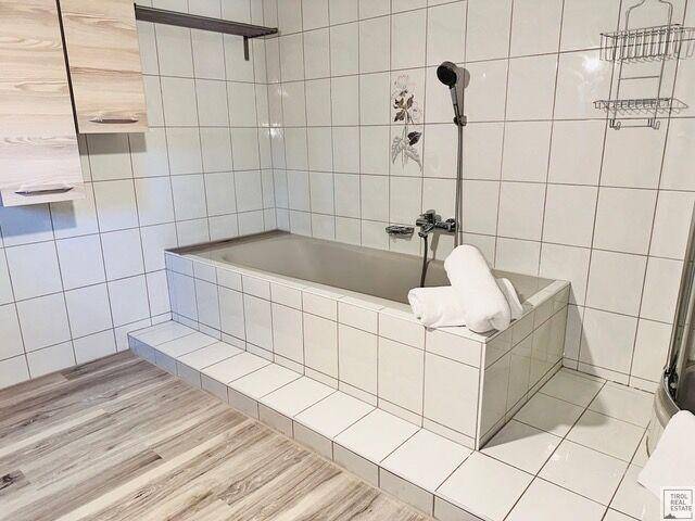 Badezimmer mit Badewanne, weißen Fliesen und Holzboden, im traditionellen Stil.