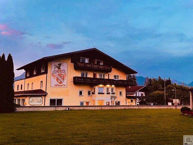 Historisches Gebäude bei Sonnenuntergang mit Wappen an der Fassade und umliegender Grünfläche.