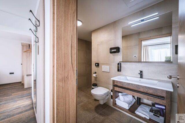 Modernes Badezimmer mit Waschtisch, Toilette und Spiegel, angrenzend an einen Flur.