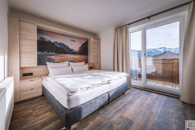 Helles Schlafzimmer mit Doppelbett, Holzboden und großem Fenster mit Panoramablick auf die Berge.