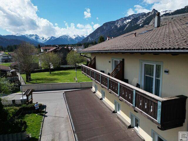 Gebäudeansicht mit mehreren Balkonen, umgeben von grünen Wiesen und einer beeindruckenden Bergkulisse.