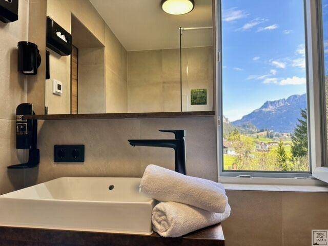 Modernes Badezimmer mit Waschtisch, Spiegel und Fenster mit Bergblick.