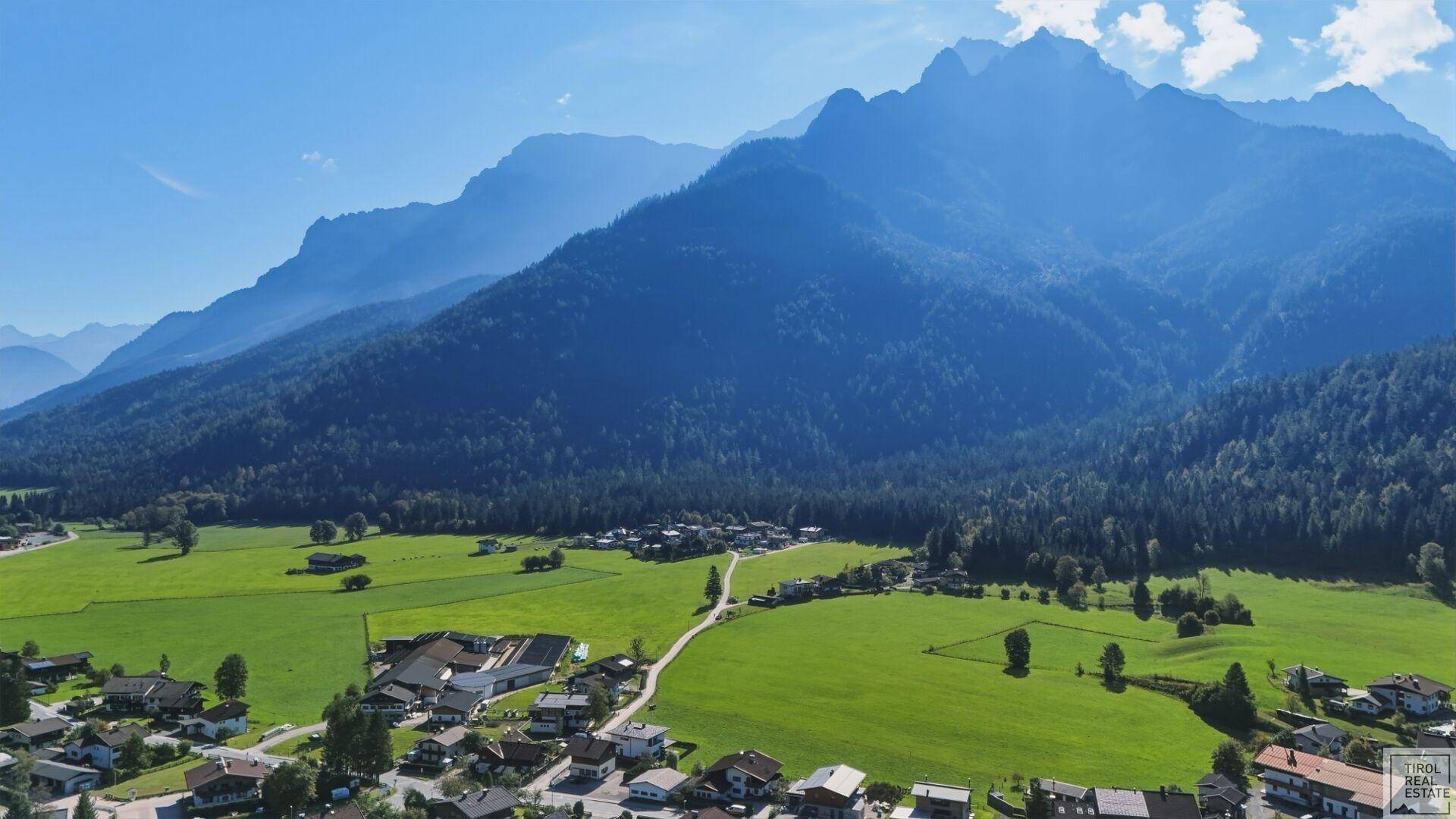 Weitwinkelaufnahme aus der Luft, die ein idyllisches Dorf vor einer beeindruckenden Bergkulisse zeigt.