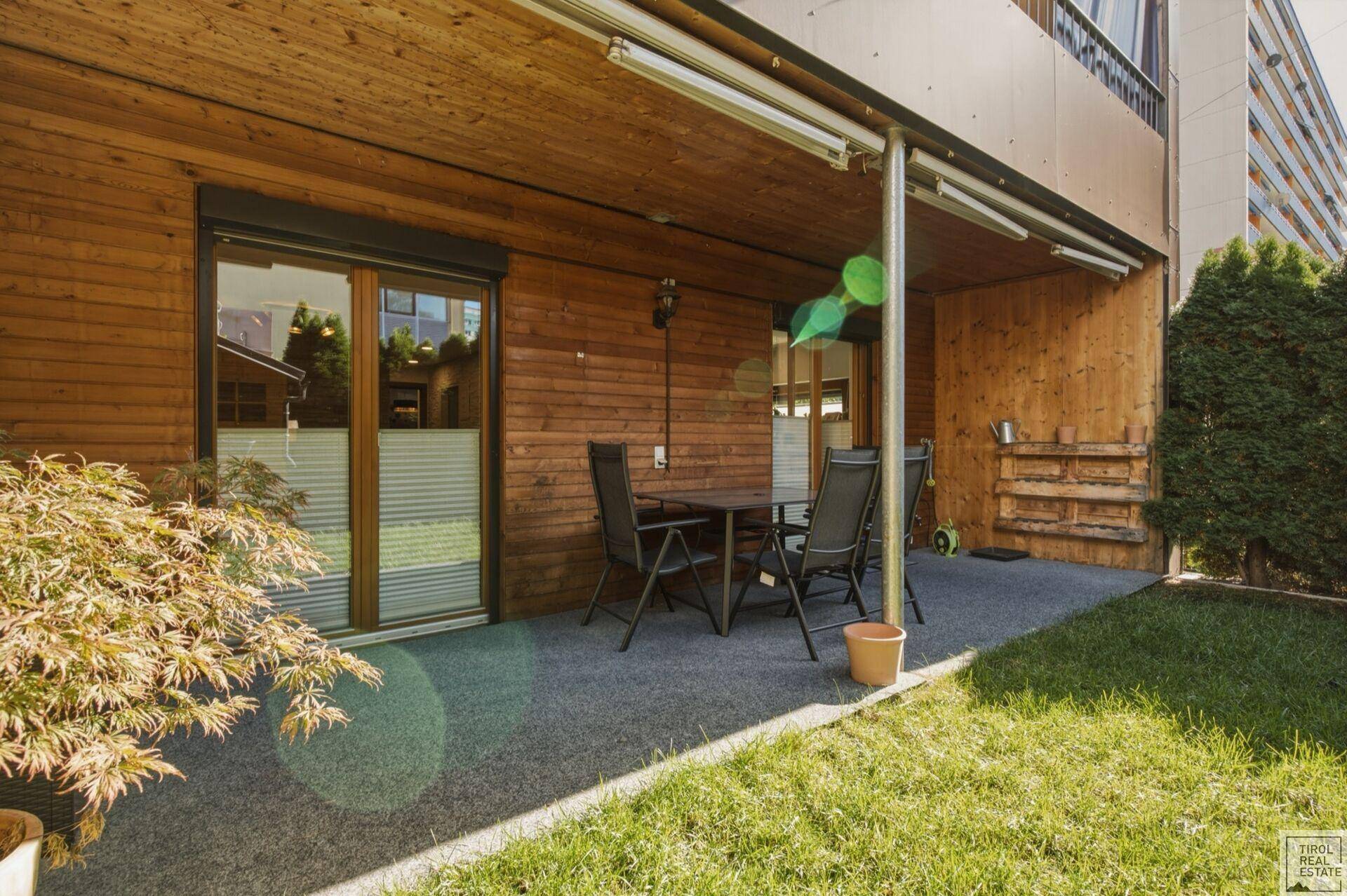 Überdachte Terrasse mit Holzwänden, Sitzgelegenheiten und Zugang zum Garten.