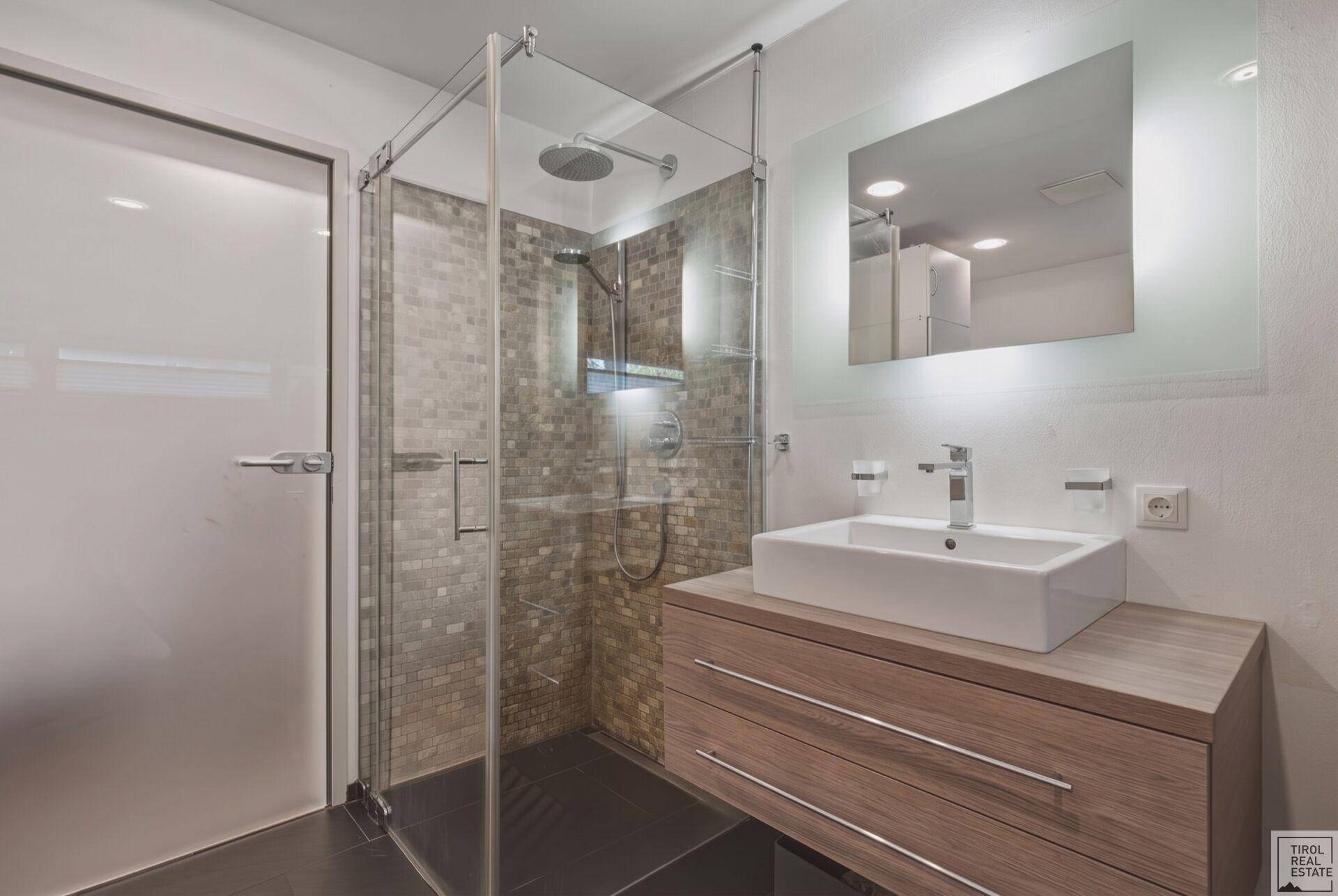 Modernes Badezimmer mit begehbarer Dusche, Waschtisch und beleuchtetem Spiegel.